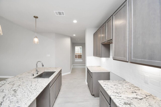 kitchen with gray cabinetry, light stone countertops, pendant lighting, backsplash, and sink