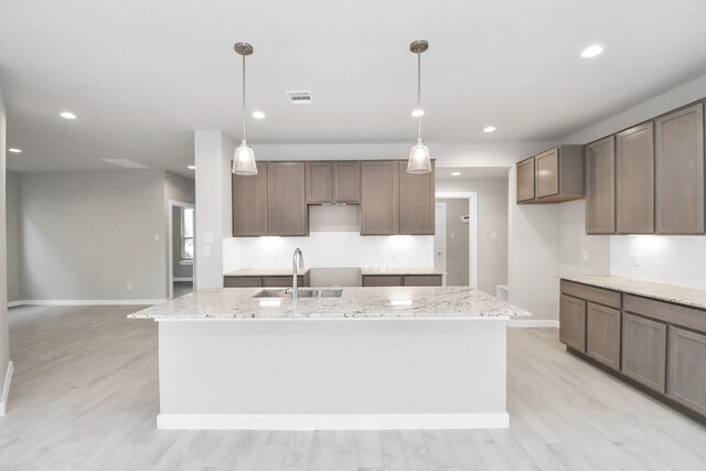 kitchen featuring light stone countertops, hanging light fixtures, an island with sink, and tasteful backsplash