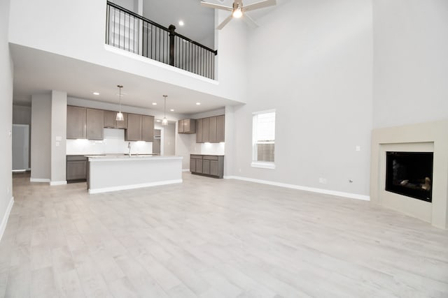 unfurnished living room with a high ceiling, ceiling fan, and light hardwood / wood-style flooring