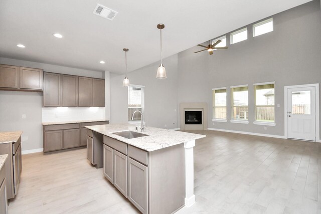 kitchen with light stone countertops, light hardwood / wood-style floors, sink, ceiling fan, and a center island with sink