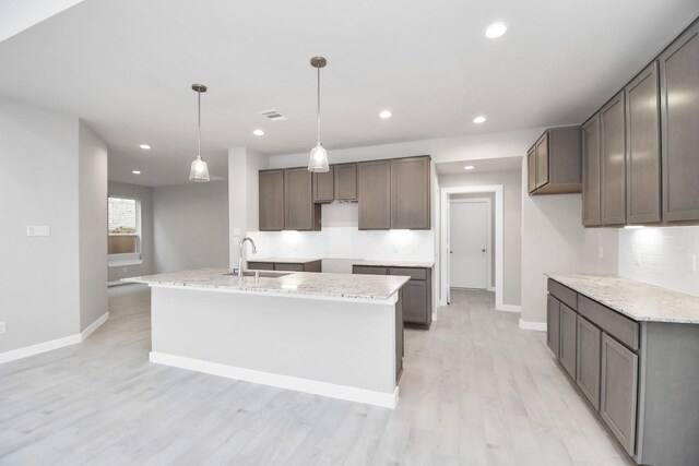 kitchen featuring light wood-type flooring, hanging light fixtures, backsplash, and light stone countertops