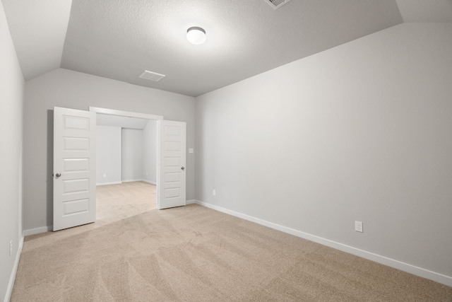 unfurnished bedroom with light carpet, lofted ceiling, and a textured ceiling