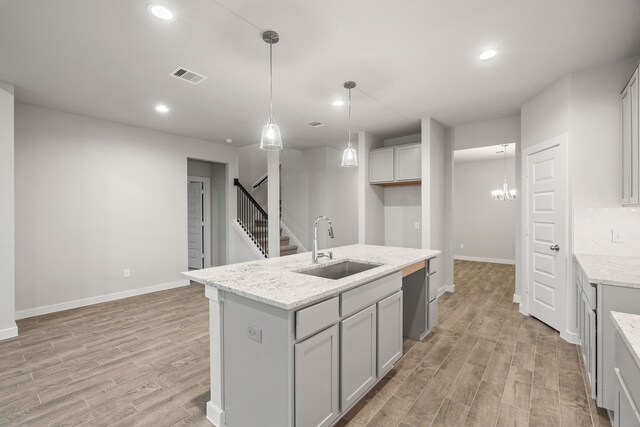 kitchen with an island with sink, pendant lighting, light stone countertops, and light hardwood / wood-style floors