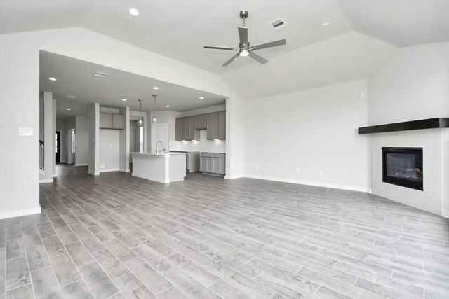 unfurnished living room with ceiling fan, sink, light wood-type flooring, and vaulted ceiling