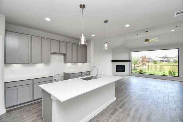 kitchen featuring gray cabinetry, an island with sink, ceiling fan, and sink