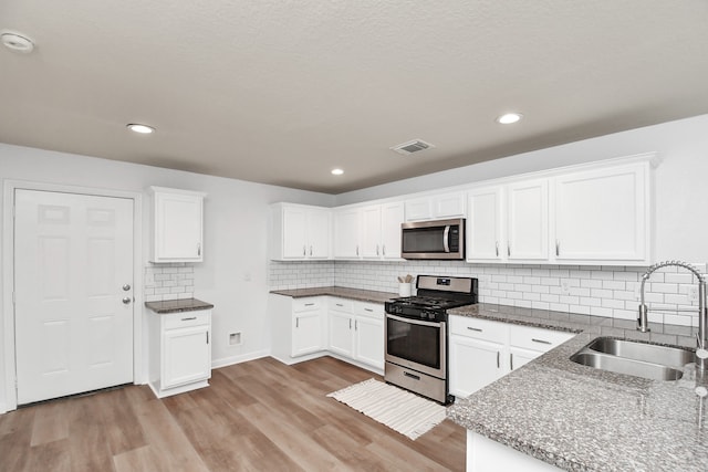 kitchen with white cabinets, appliances with stainless steel finishes, light hardwood / wood-style floors, sink, and tasteful backsplash