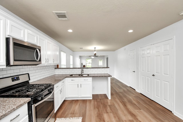 kitchen featuring white cabinets, backsplash, light wood-type flooring, appliances with stainless steel finishes, and sink