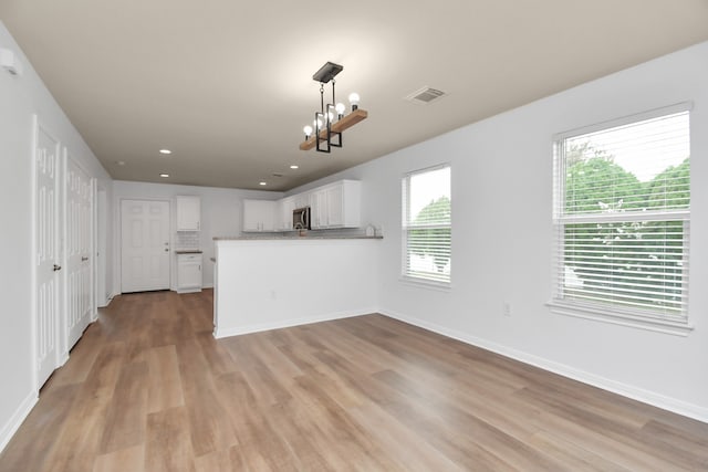 unfurnished living room with light wood-type flooring and an inviting chandelier