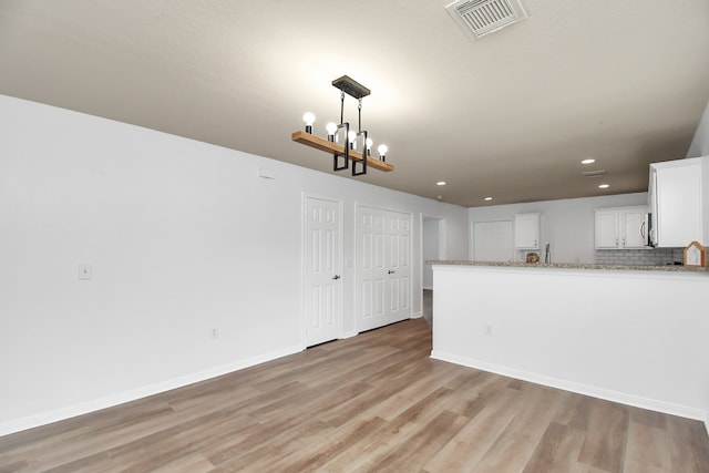 kitchen with light wood-type flooring, white cabinetry, backsplash, light stone counters, and an inviting chandelier