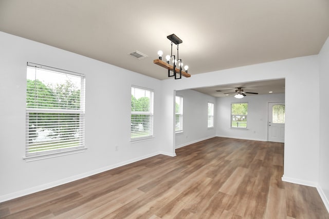 spare room with ceiling fan with notable chandelier, hardwood / wood-style flooring, and plenty of natural light