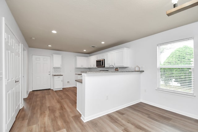 kitchen with kitchen peninsula, hardwood / wood-style flooring, white cabinets, and tasteful backsplash