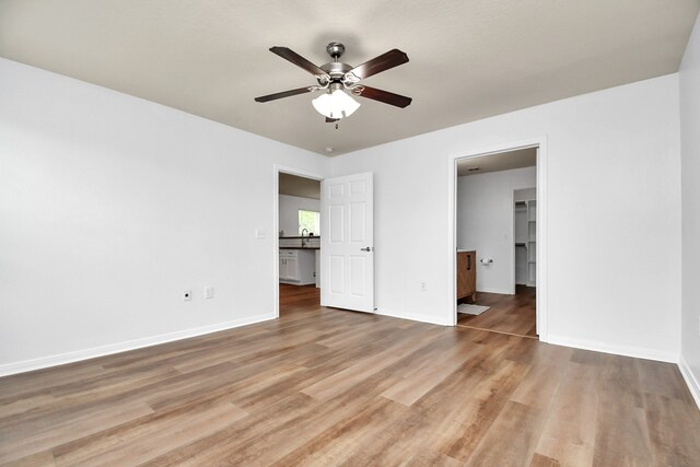 unfurnished bedroom featuring wood-type flooring, a walk in closet, and ceiling fan