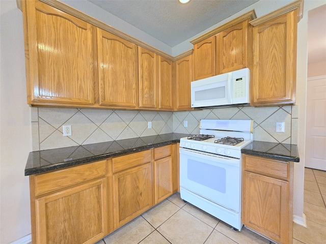 kitchen with decorative backsplash, light tile patterned flooring, white appliances, and dark stone countertops