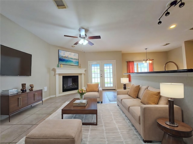 tiled living room featuring french doors and ceiling fan with notable chandelier