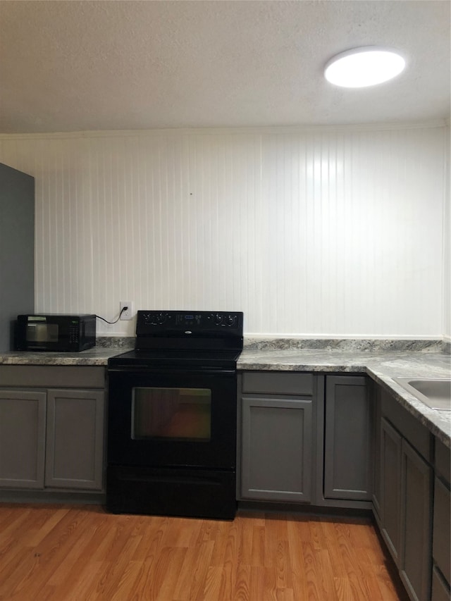 kitchen with wood walls, light wood-type flooring, black appliances, light stone countertops, and a textured ceiling