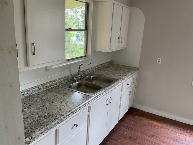 kitchen with light stone countertops, white cabinetry, dark hardwood / wood-style floors, and sink