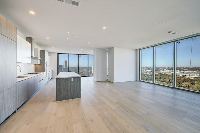 kitchen with a wall of windows, wall chimney exhaust hood, a center island, and light wood-type flooring