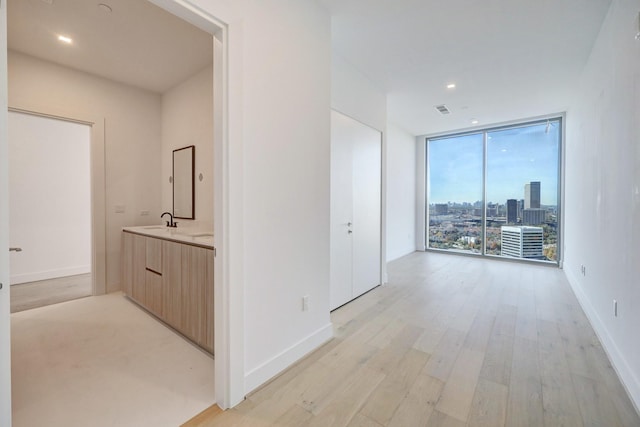 corridor with expansive windows, sink, and light hardwood / wood-style flooring