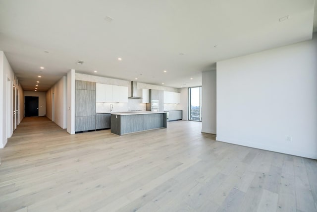 kitchen with white cabinets, wall chimney exhaust hood, a center island, and light hardwood / wood-style floors