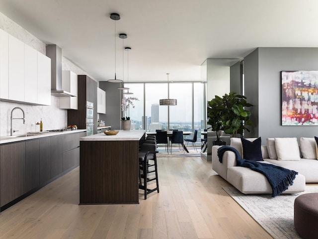 kitchen with pendant lighting, wall chimney exhaust hood, white cabinets, and dark brown cabinets