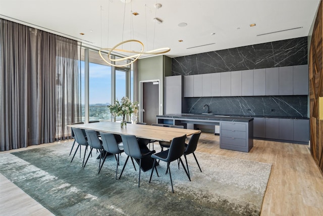 dining room featuring an inviting chandelier, sink, a wall of windows, and light wood-type flooring