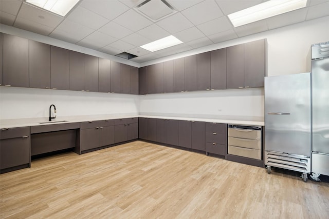 kitchen featuring sink, light hardwood / wood-style flooring, stainless steel built in fridge, and a paneled ceiling
