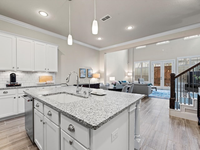 kitchen with white cabinets, a center island with sink, sink, and decorative light fixtures