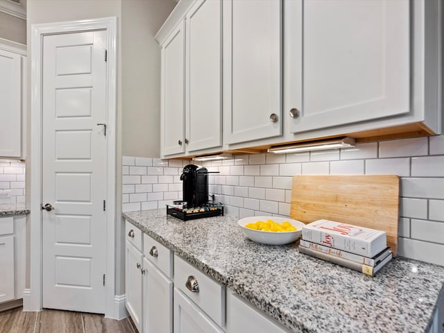 kitchen with light stone countertops, decorative backsplash, light hardwood / wood-style floors, and white cabinets