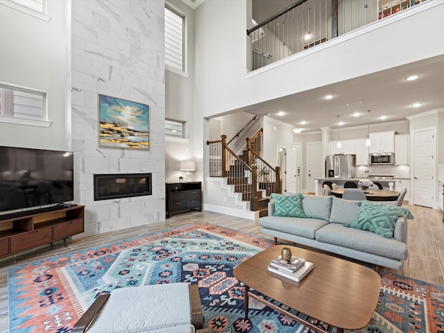 living room with a large fireplace, crown molding, a towering ceiling, and light hardwood / wood-style floors