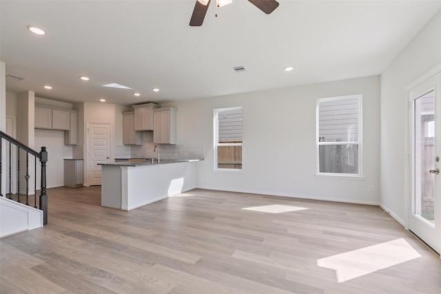 kitchen with visible vents, a peninsula, light wood-style flooring, a sink, and tasteful backsplash