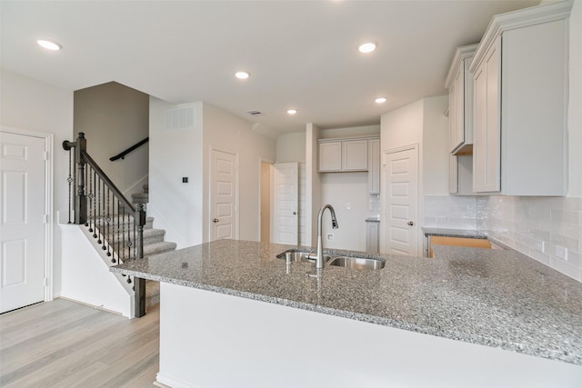 kitchen with visible vents, stone counters, a sink, light wood-style floors, and backsplash