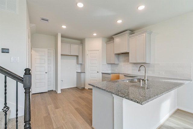 kitchen with visible vents, light wood-style flooring, a sink, a peninsula, and stone counters