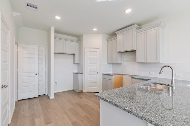 kitchen featuring visible vents, a sink, light wood finished floors, stone counters, and decorative backsplash