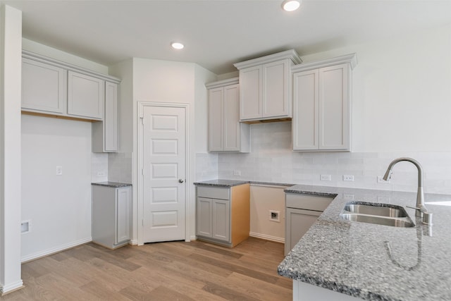 kitchen featuring backsplash, light wood-style floors, stone counters, and a sink