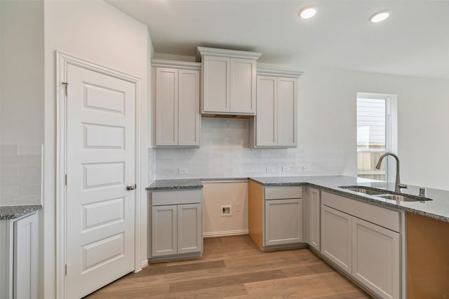 kitchen with light wood finished floors, decorative backsplash, recessed lighting, stone countertops, and a sink