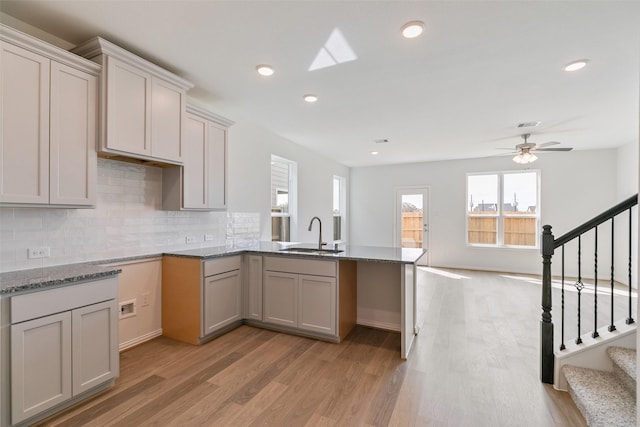 kitchen with a sink, recessed lighting, a peninsula, light wood finished floors, and decorative backsplash