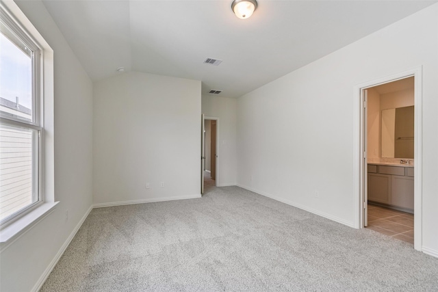 empty room with visible vents, light carpet, baseboards, and vaulted ceiling