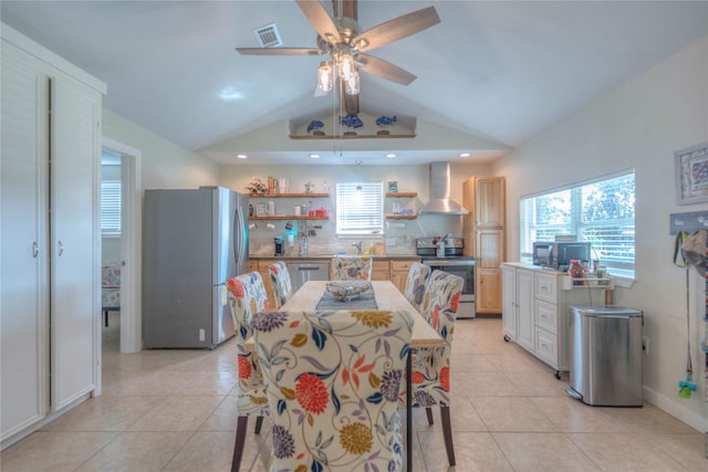 kitchen featuring appliances with stainless steel finishes, light tile patterned floors, vaulted ceiling, and wall chimney exhaust hood