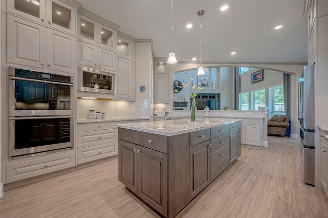 kitchen featuring decorative light fixtures, appliances with stainless steel finishes, light stone counters, and a center island