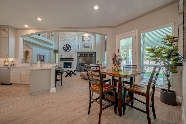 dining area with a stone fireplace, light hardwood / wood-style floors, and ornamental molding