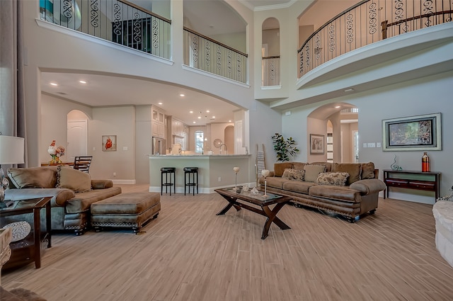 living room with a towering ceiling, light hardwood / wood-style floors, and ornamental molding