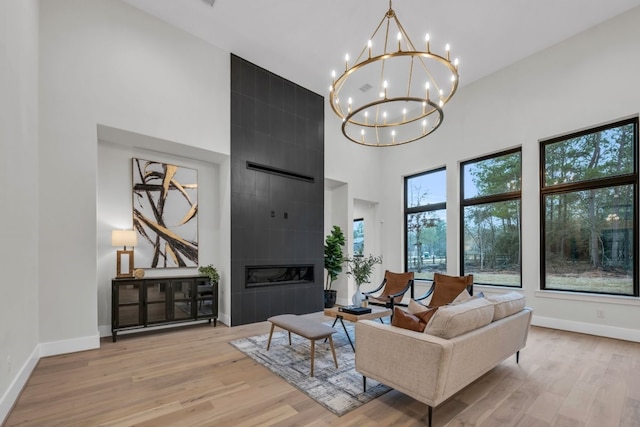 living room with a high ceiling, a tiled fireplace, a notable chandelier, and light hardwood / wood-style floors