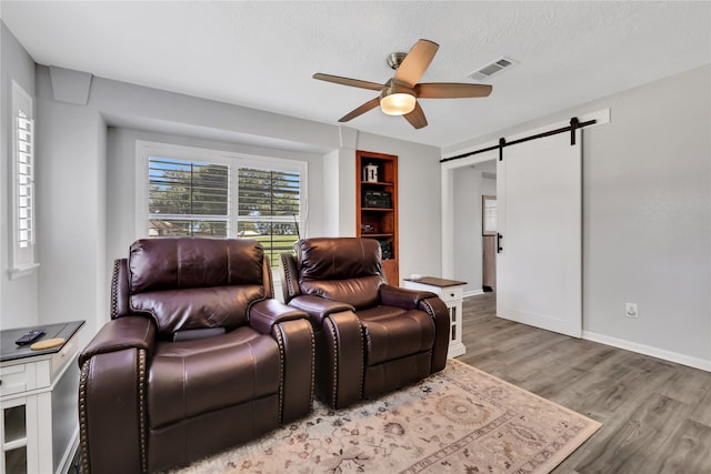 cinema with a barn door, ceiling fan, light wood-type flooring, and a textured ceiling