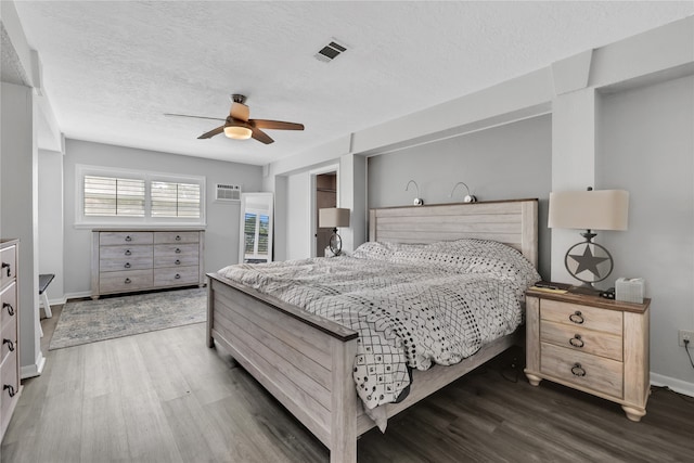 bedroom with a textured ceiling, dark wood-type flooring, ceiling fan, and a wall unit AC