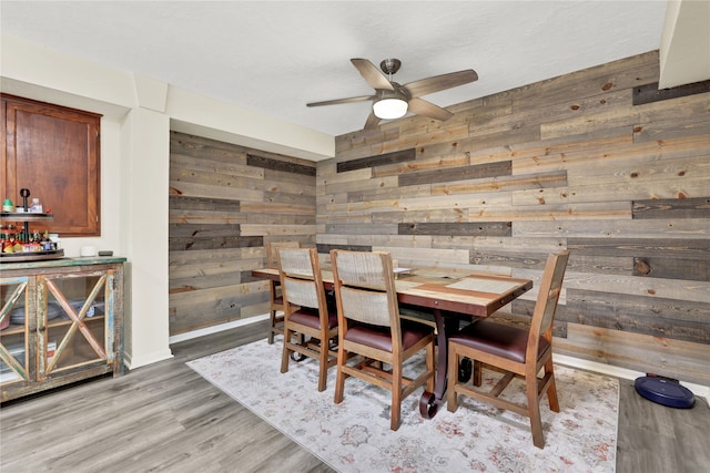 dining space with hardwood / wood-style floors, ceiling fan, and wooden walls