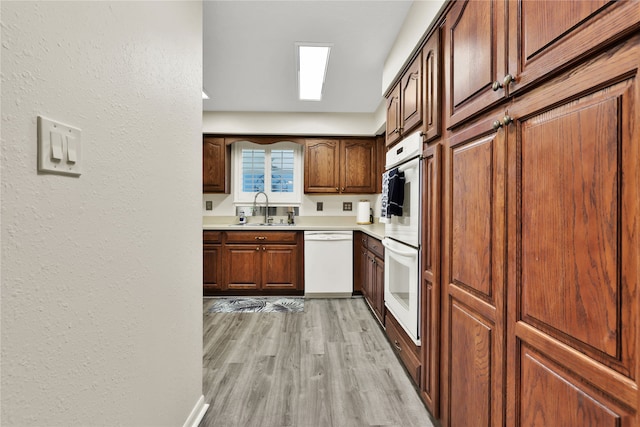 kitchen featuring dishwasher, sink, light wood-type flooring, and a skylight