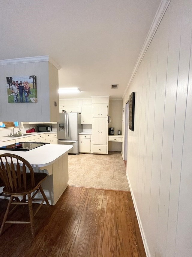 kitchen featuring black appliances, kitchen peninsula, ornamental molding, light wood-type flooring, and white cabinets