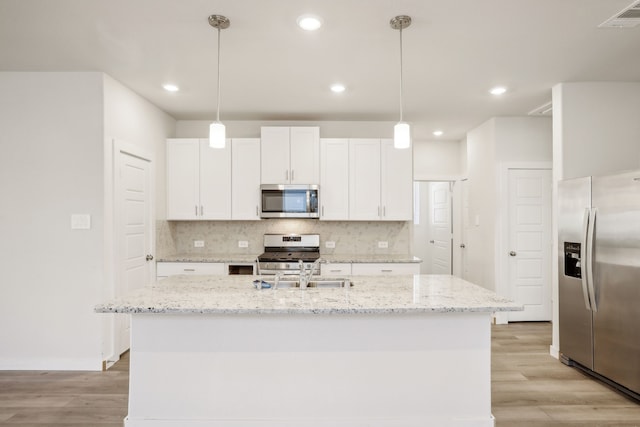 kitchen featuring decorative light fixtures, white cabinetry, appliances with stainless steel finishes, and a kitchen island with sink