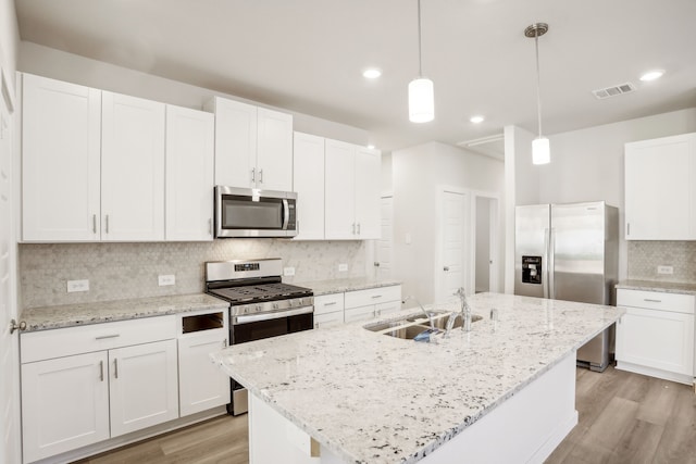 kitchen with decorative light fixtures, sink, white cabinets, an island with sink, and stainless steel appliances