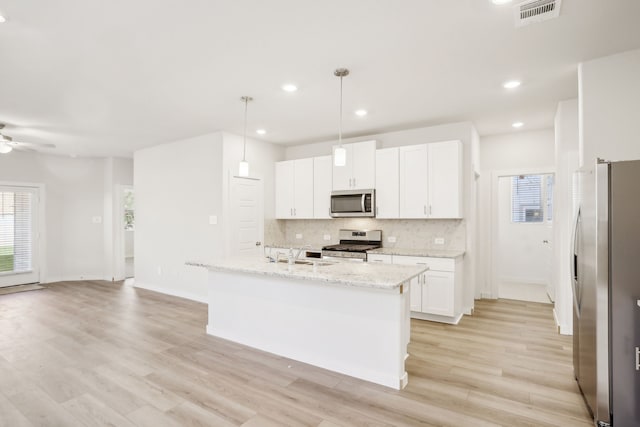 kitchen with decorative light fixtures, white cabinets, a center island with sink, decorative backsplash, and stainless steel appliances